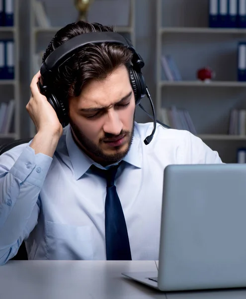 Joven en el concepto de centro de llamadas trabajando hasta tarde horas extras en la oficina —  Fotos de Stock