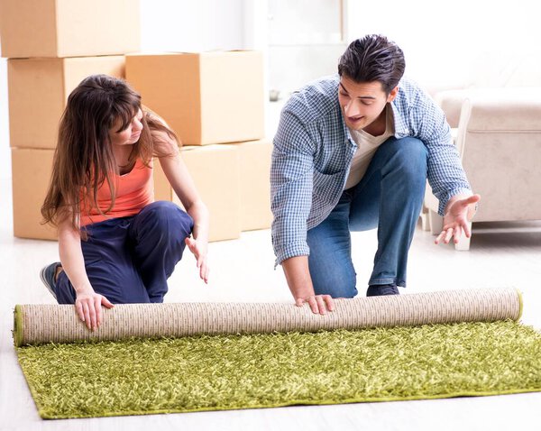 Young family rolling carpet at new apartment