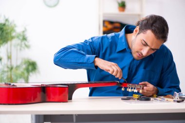 Gitarı tamir eden genç bir erkek tamirci.