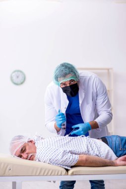 Yaşlı adam genç erkek stajyer doktoru ziyaret ediyor.