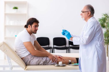 Yaralı adam ilk yardım konseptinde yaşlı doktoru ziyaret ediyor.