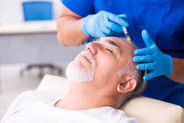 Yaşlı adam saç nakli için genç erkek doktoru ziyaret ediyor.