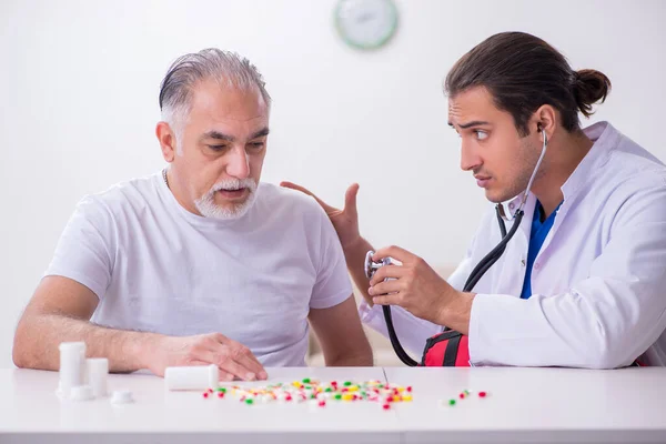 Jonge mannelijke arts bezoekt oude mannelijke patiënt thuis — Stockfoto