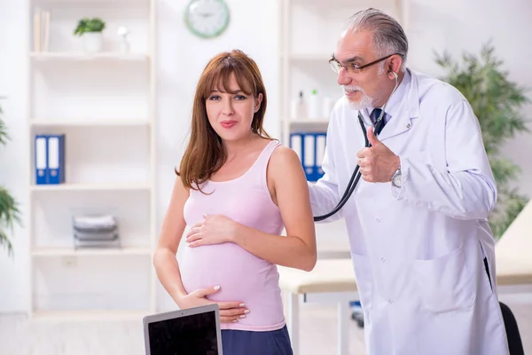 Jovem mulher grávida visitando velho médico ginecologista masculino — Fotografia de Stock