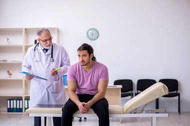 Genç erkek hasta yaşlı erkek doktoru ziyaret ediyor.
