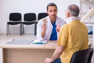 Yaşlı boynu yaralı bir adam genç erkek doktoru ziyaret ediyor.