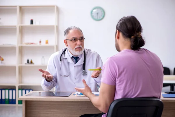 Jovem paciente masculino visitando velho médico masculino — Fotografia de Stock