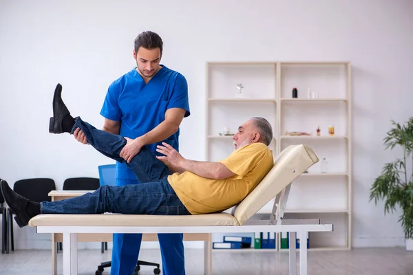 Old injured man visiting young male doctor chiropractor
