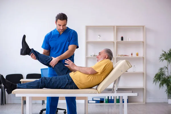 Vecchio ferito visitando giovane medico chiropratico maschile — Foto Stock