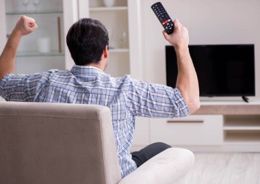 Genç adam evde televizyon izliyor.