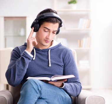 Genç adam kitap okuyor ve sesli kitap dinliyor.