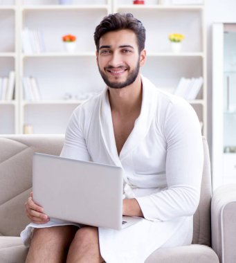 Genç adam evde dizüstü bilgisayarla çalışıyor.