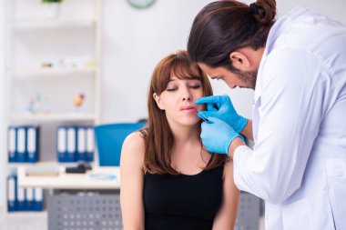 Genç bir kadın erkek doktor dermatoloğunu ziyaret ediyor.