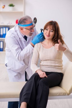 Genç bir kadın yaşlı erkek doktor otorhinolaryngologist 'i ziyaret ediyor.