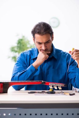 Gitarı tamir eden genç bir erkek tamirci.