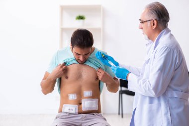 Yaralı genç adam deneyimli erkek doktoru ziyaret ediyor.