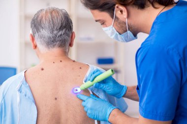 Yaşlı adam genç erkek doktor dermatoloğu ziyaret ediyor.