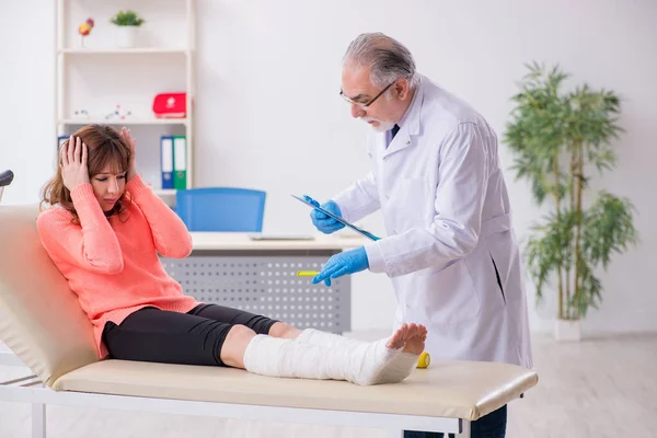 Giovane gamba ferita donna visita vecchio medico traumatologo — Foto Stock