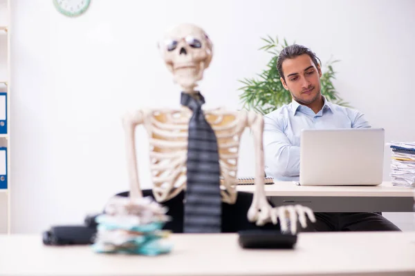 Young male employee and skeleton in the office — Stock Photo, Image