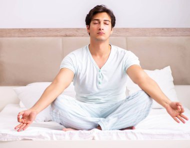Genç adam yatakta yoga yapıyor.