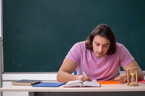 Jonge mannelijke student in het klaslokaal op tijdmanagementconcept — Stockfoto