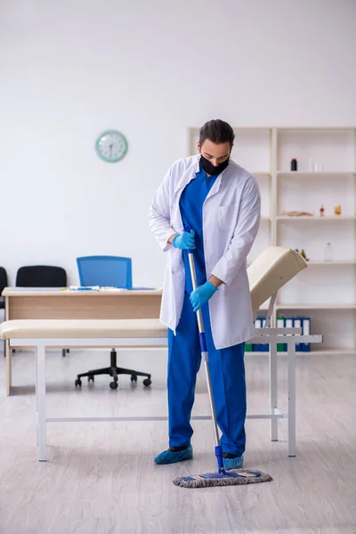 Joven contratista masculino desinfectando clínica en concepto pandémico — Foto de Stock