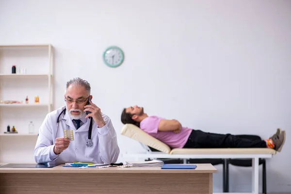 Giovane paziente maschio visita vecchio medico maschio — Foto Stock