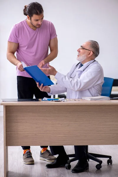 Genç erkek hasta yaşlı erkek doktoru ziyaret ediyor. — Stok fotoğraf