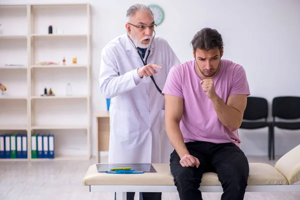 Jonge mannelijke patiënt bezoekt oude mannelijke arts — Stockfoto