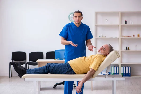 Vecchio ferito visitando giovane medico chiropratico maschile — Foto Stock