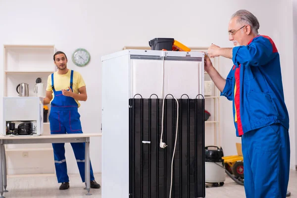 Two contractors repairing fridge at workshop