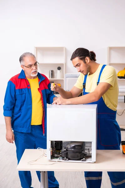 Two contractors repairing fridge at workshop