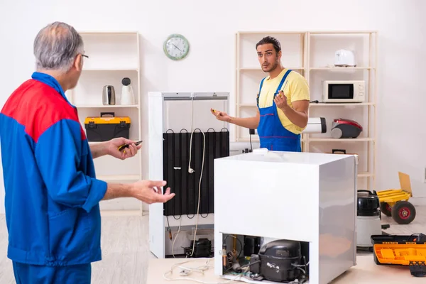 Two contractors repairing fridge at workshop