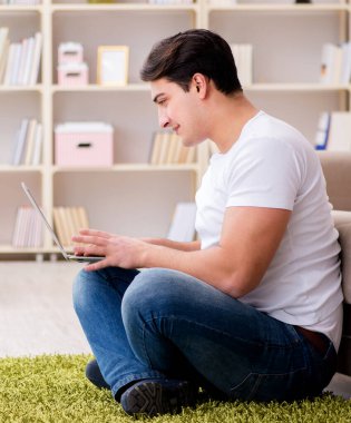 Evde, halı döşemesinde dizüstü bilgisayarda çalışan bir adam.