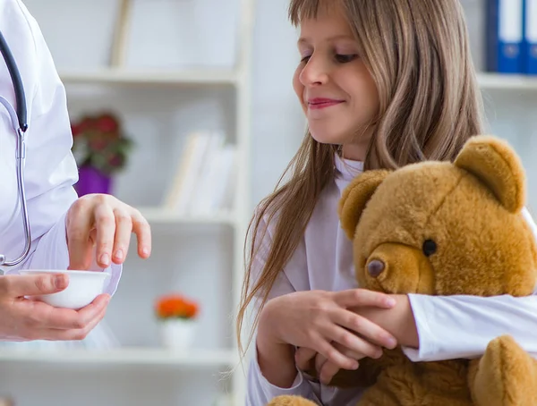 Mulher médica examinando pouco bonito menina com urso de brinquedo — Fotografia de Stock