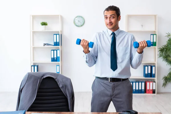 Jovem e bonito funcionário fazendo exercícios esportivos no local de trabalho — Fotografia de Stock