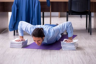 Genç yakışıklı işadamı iş yerinde egzersiz yapıyor.