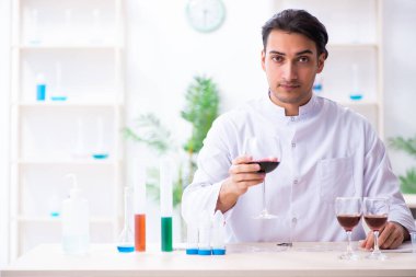 Erkek kimyager laboratuvarda şarap örneklerini inceliyor.