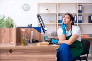 Genç yakışıklı müteahhit ofisi temizliyor.