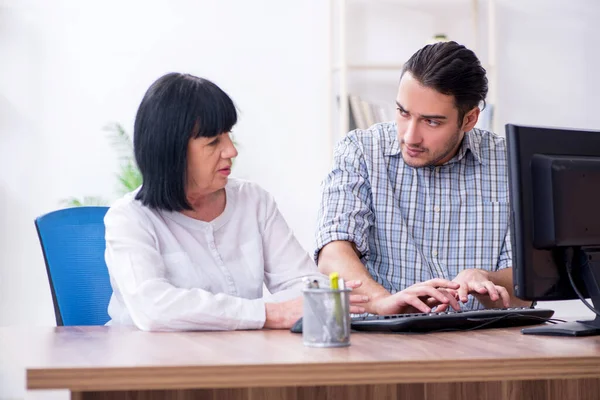 Young male employee explaining to old female colleague how to us — Stock Photo, Image