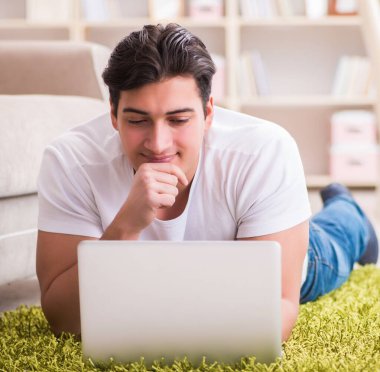 Evde, halı döşemesinde dizüstü bilgisayarda çalışan bir adam.