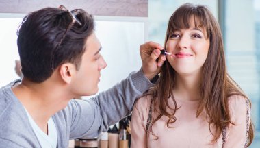 Güzellik salonunda güzel bir kadın için makyaj yapan adam.