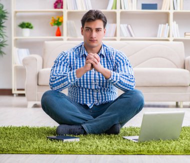 Genç yakışıklı adam evde yerde oturuyor.