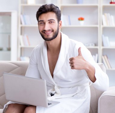 Genç adam evde dizüstü bilgisayarla çalışıyor.