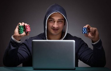 Kapüşonlu genç adam dizüstü bilgisayarın önünde oturuyor.