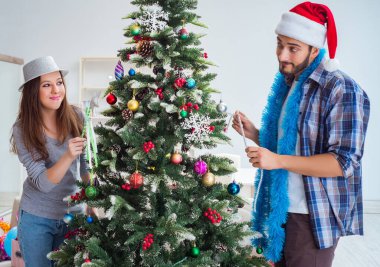 Genç aile Noel ağacını mutlu bir vesileyle süslüyor.