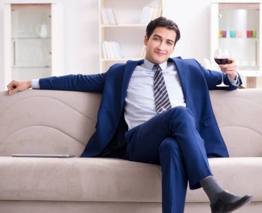 İş adamı evde oturmuş şarap içiyor.
