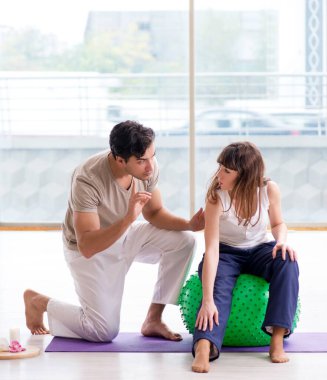 Kişisel koç, jimnastik salonunda denge topuyla kadınlara yardım ediyor.