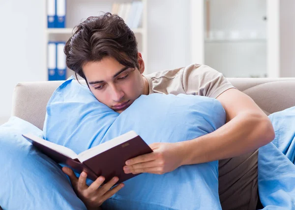 Üniversite sınavlarına hazırlanan genç bir öğrenci kitapla yatakta.