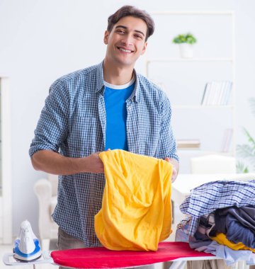 Genç adam evde çamaşır ütülüyor.